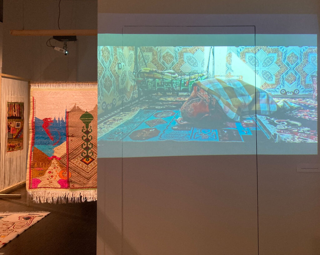 Auf einem Video ist zu sehen, wie eine Frau an einem Teppich arbeitet, im Rautenstrauch-Joest-Museum