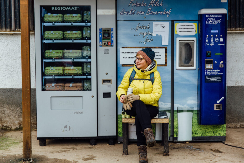 Frau sitzt vor einem Automaten, an dem Milch in Flaschen abgezapft werden kann
